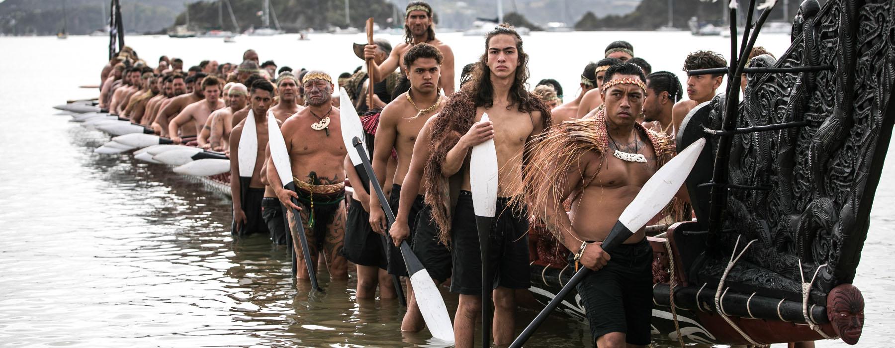 A group of Māori men lift a waka onto the shore