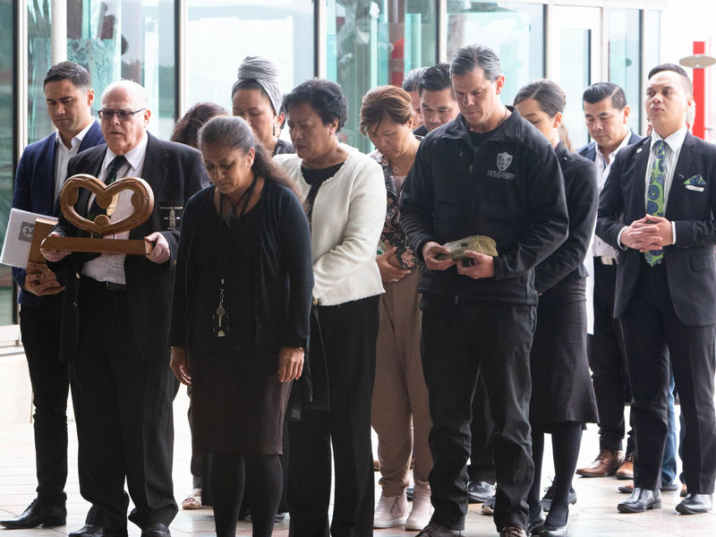 A group of people, one person is holding the pin which sits on a piece of pounamu