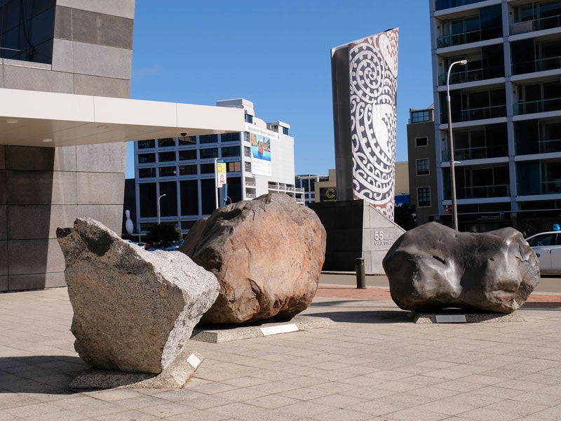 Entrance boulders, 2017. Photograph by Rachael Hockridge. Te Papa Three large rocks on a tiled forecourt. There are buildings and a plinth in the background.