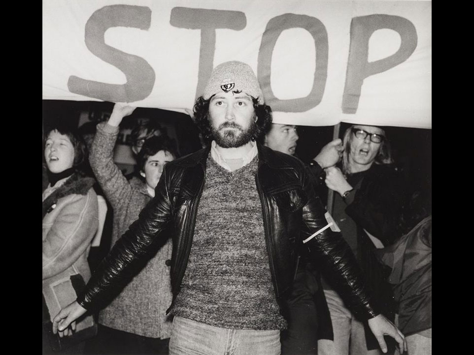 A man stands in front of a sign which says 'stop'