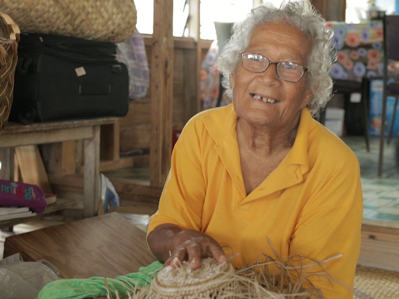 A lady in a yellow shirt holds up some of her weaving