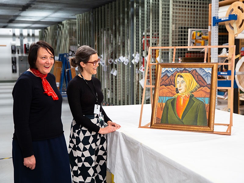 Head of Art Charlotte Davy and Curator Modern Art Lizzie Bisley with Rita Angus, Marjorie Marshall, 1938/39. Photo by Jack Fisher. Te Papa Two women in a painting store room look at a painting on display on a table