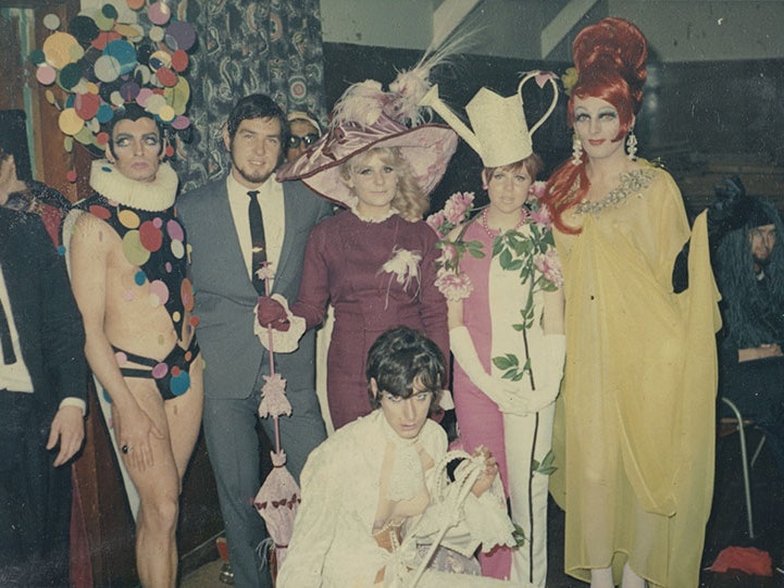 Drag performers. From the album: Johnny Croskery photograph album 1960-1980, 1960-1980, New Zealand, maker unknown. Te Papa (O.044386) Group of people in flamboyant costume in an array of colours and styles pose for a photo