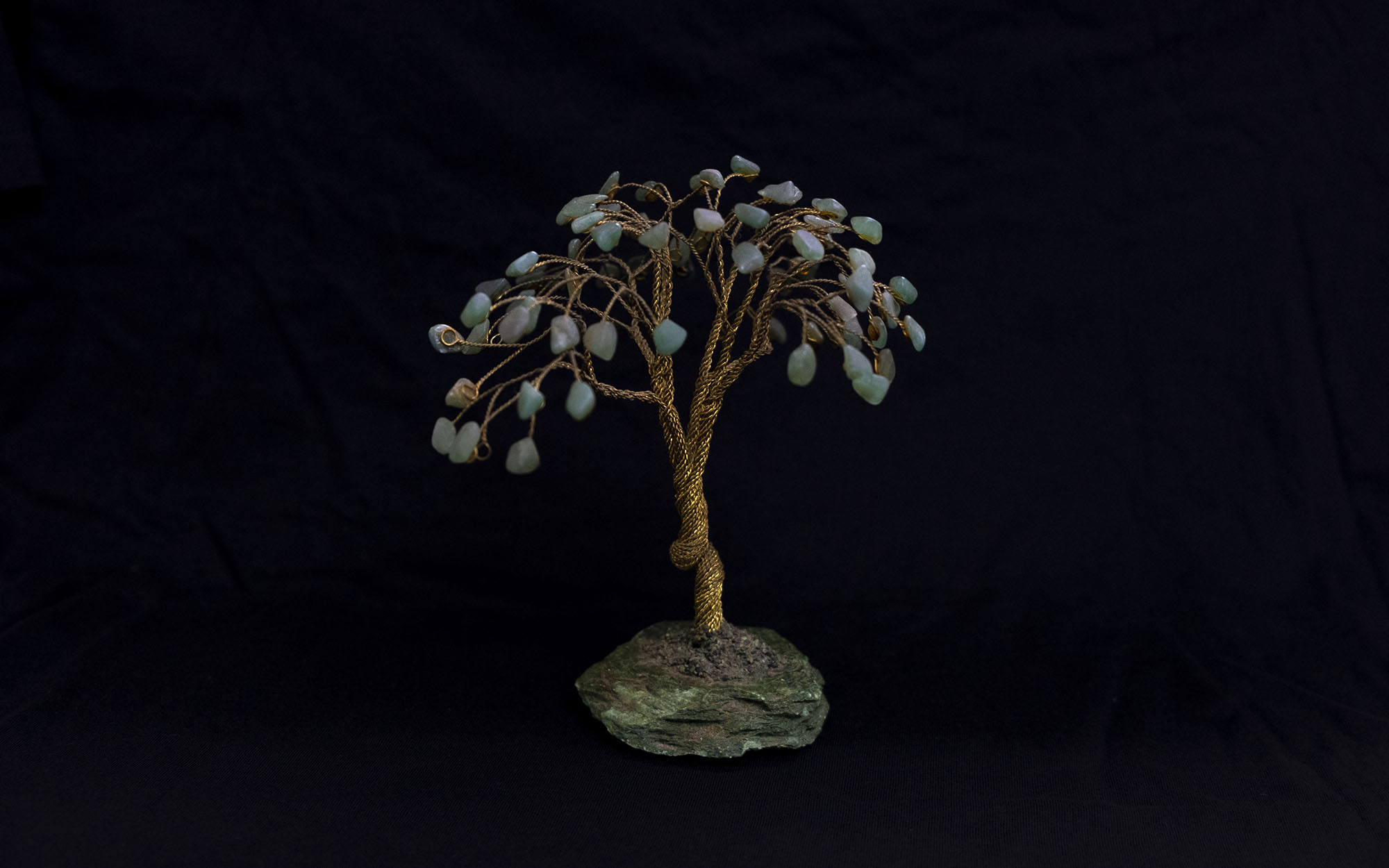 An ornamental tree made of gold-coloured wire, sitting on a rock, with crystals hanging from the branches to represent leaves