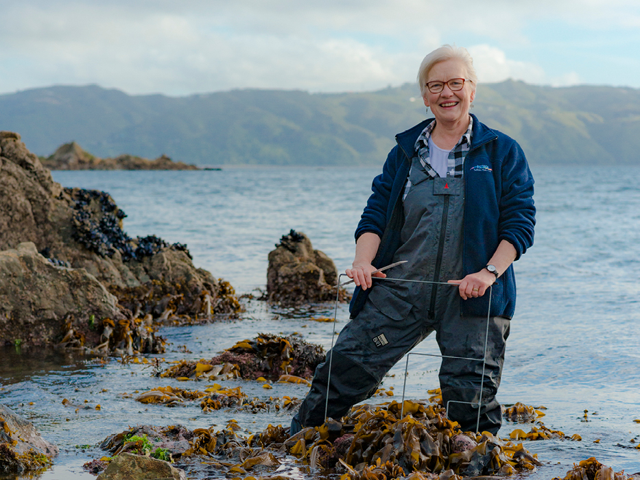 A woman in overalls is standing in a rockpool by the ocean.