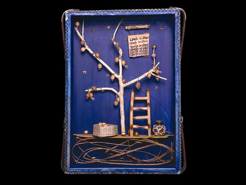 Lauren Lysaght, L’albero della famiglia (The family tree), from the series Hidden Agender, 1993, wood, cane, seagrass, metal, ceramic, perspex, paint. Purchased 1993 with New Zealand Lottery Grants Board funds. Te Papa (1993-0022-1) A blue box containing a wooden tree with apples, a ladder to climb to the branches, a basket for the apples, and a sign repeating uno/una in dieci (Italian for one in ten)