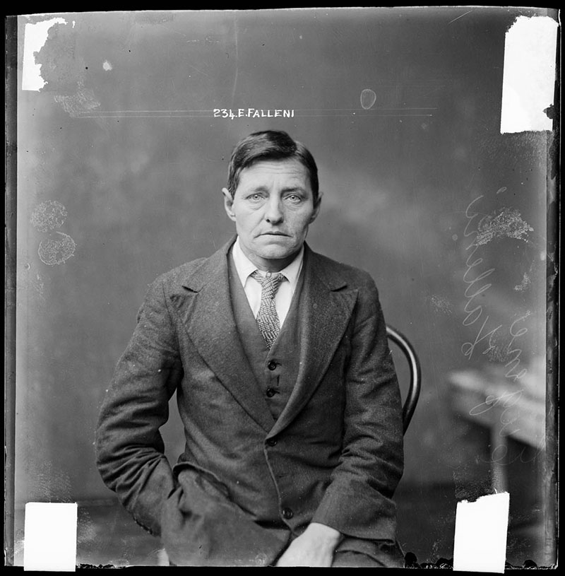 Police photo of Eugenia, dressed in a suit and sitting on a chair, with a stern look on her face