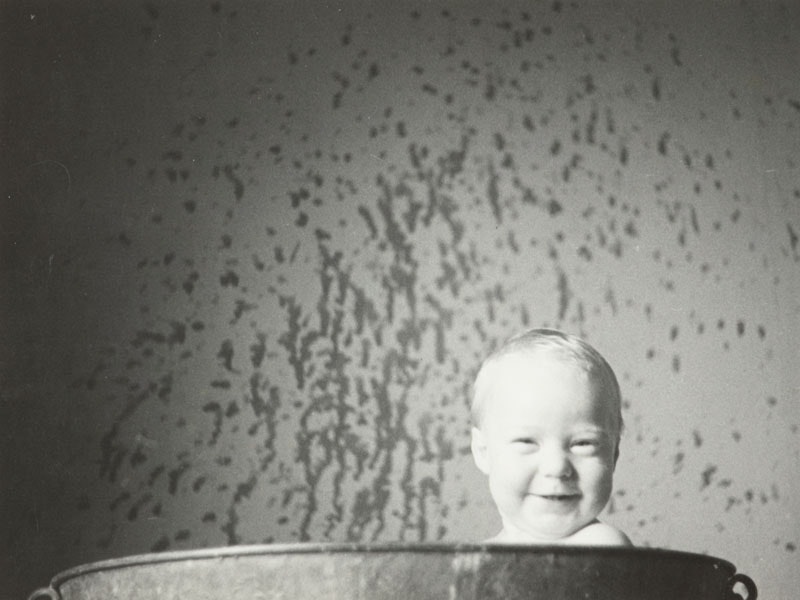 Peter Lee-Johnson in the bath, Piha, 1940s, North Island, by Eric Lee-Johnson. Purchased 1997 with New Zealand Lottery Grants Board funds. © Te Papa. CC BY-NC-ND 4.0. Te Papa (O.008135) A baby grins, he's poking his head above a bathtub. There's water splashes on the walls.
