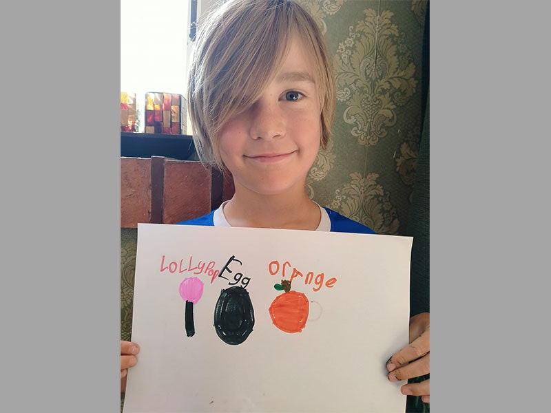 Leo and his self-portrait, 2020. Photo by Martin Langdon. Te Papa Boy holds sheet of paper. On the paper he has drawn a lollipop, and egg, and an orange to represent the letters of his name