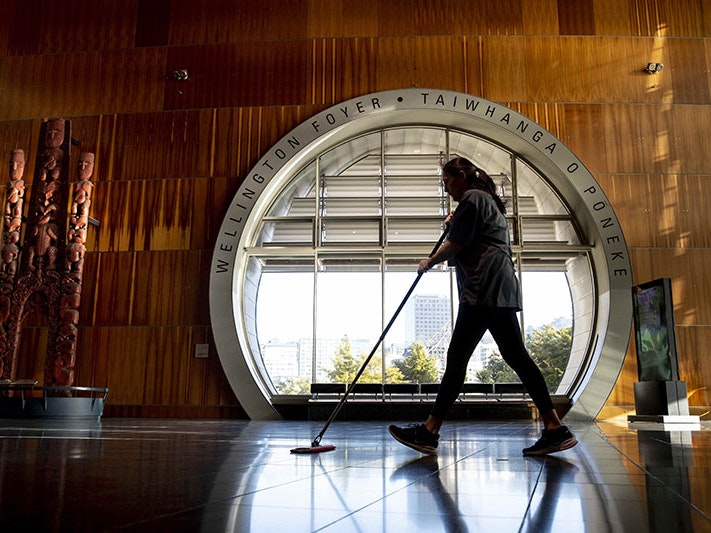Cleaner Kellie Tapuae is one of the essential workers taking care of Te Papa while it is closed to the public. Wellington Foyer, 2020. Photo by Maarten Holl. Te Papa A woman wiping the floor passes a large round window in the Te Papa foyer