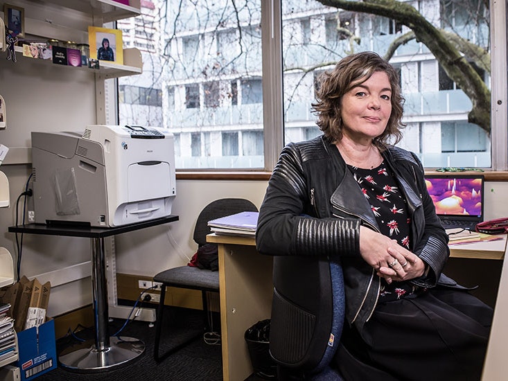 Professor Juliet Gerrard, 2018. Photo by Simon Young / simonyoungphotographer.com Juliet sits at her desk, with her arm over the back of the chair, in her office. Behind her is a large printer and shelves with books and framed photos