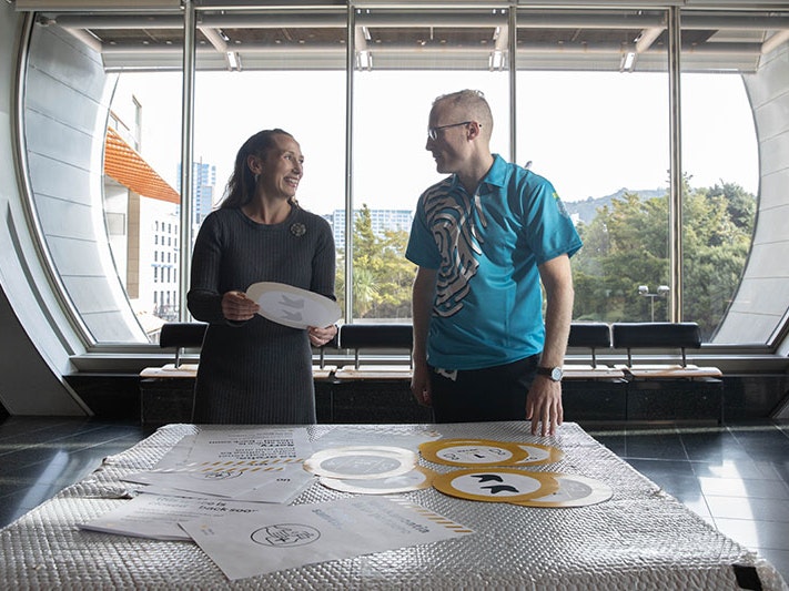 Chief Executive Courtney Johnston and Head of Visitor Services Shaun Pallett review information posters about Te Papa’s new hygiene measures. Photo by Jack Fisher. Te Papa Two people stand in front of a table with an array of safety notices on it