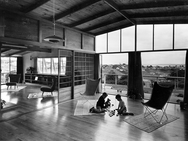 Sparrow Industrial Pictures, Interior of Catley House, designed by Bill Wilson, about 1953, copy of original photograph. Penman Family Collection. Black and white photo of two children playing on the floor in a big room with a view of other houses and the harbour.