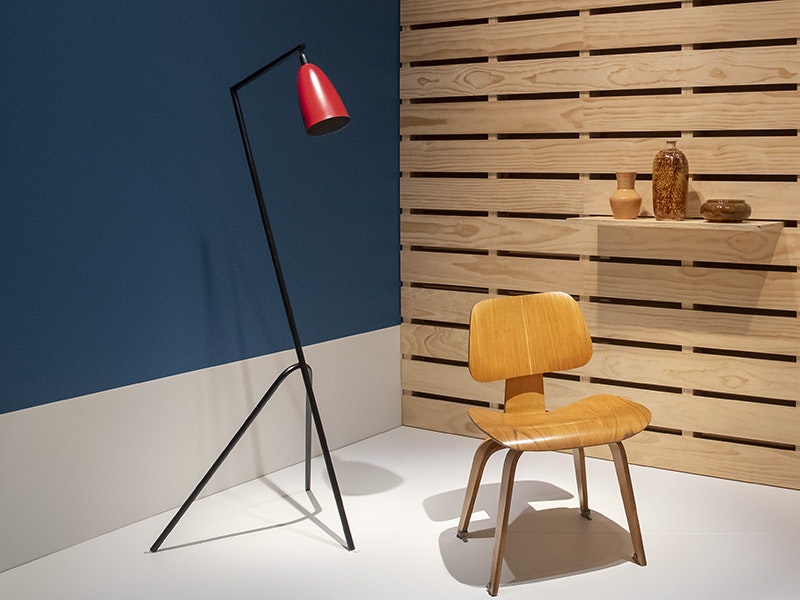 Installation shot of Modern Living: Design in 1950s New Zealand | Te Noho Hou: Te Hoahoa ki Aotearoa i ngā tau 1950 exhibition, Toi Art. Photo by Maarten Holl / Te Papa, 2020. a lamp, and a chair on a blue and wooden platform