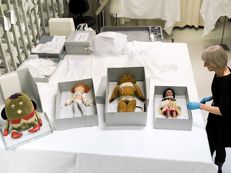 A woman in a black dress working with four toys in separate white boxes on a table