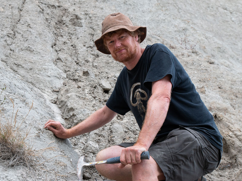 Alan on a steep gravel bank, he has a pickaxe in his hand