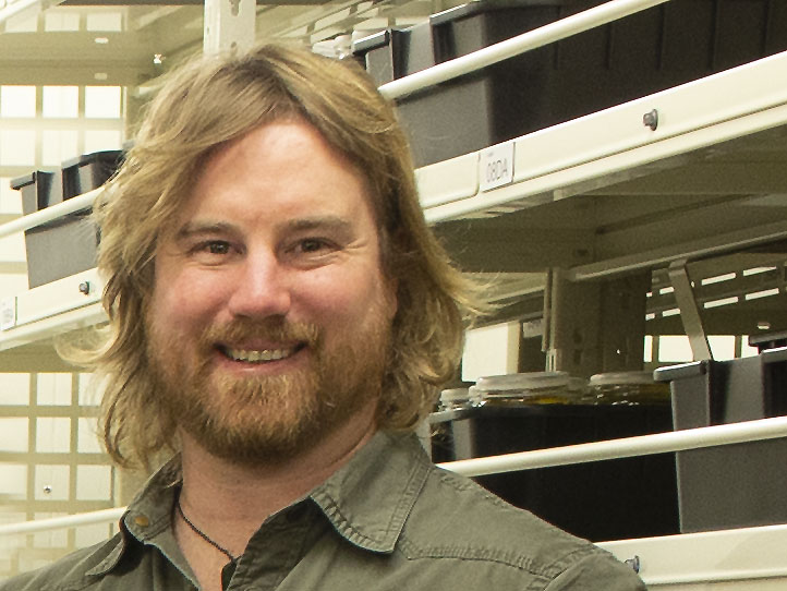 A closeup of a bearded man standing in front of jars of fish