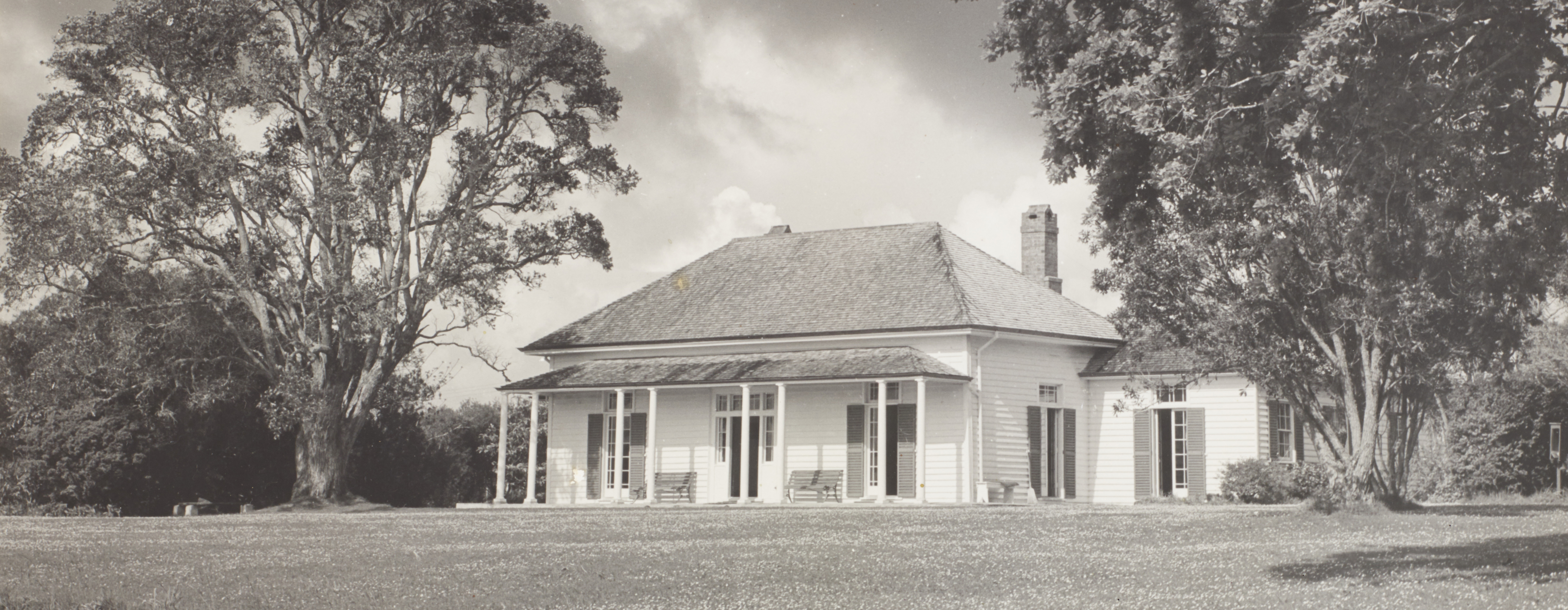 A one-storey house between to large trees with a mowed lawn in the forground