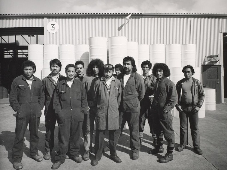 10.5.1982. Rheem Industries, Rosebank Road, Avondale, west Auckland. 44 gallon drum assembly line workers by Mark Adams, 1982. Purchased 1993 with New Zealand Lottery Grants Board funds. Te Papa (O.004103) Black and white photo of 11 men in overalls standing in front of a factory