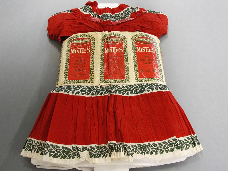 Costume, child's (dress and hat made out of Minties labels), circa 1927, maker unknown. Gift of Shelley Venimore (née O'Brien), 2011. CC BY-NC-ND 4.0. Te Papa (GH017183) A photo of a red child's dress made with Mintie sweet wrapper paper and material