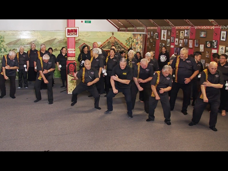 Still from video courtesy of Taranaki ki te Tonga Taikura People in a large room performing a dance with actions