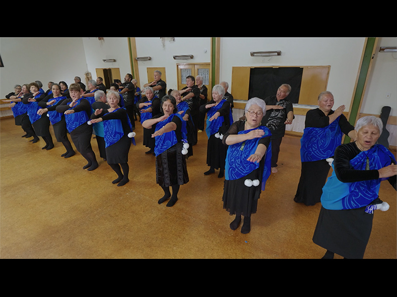 People in a large room performing a dance with actions