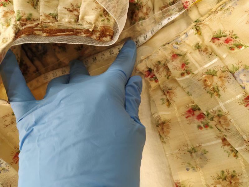 A blue-gloved hand holding a measuring tape down on a piece of fabric that is yellow with small red flowers