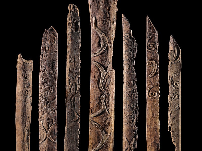 Composite image of Moriori whare carvings. Photo by Norm Heke. Te Papa (MA_I.006386) A black background with seven posts of varying height showing carvings on each one.