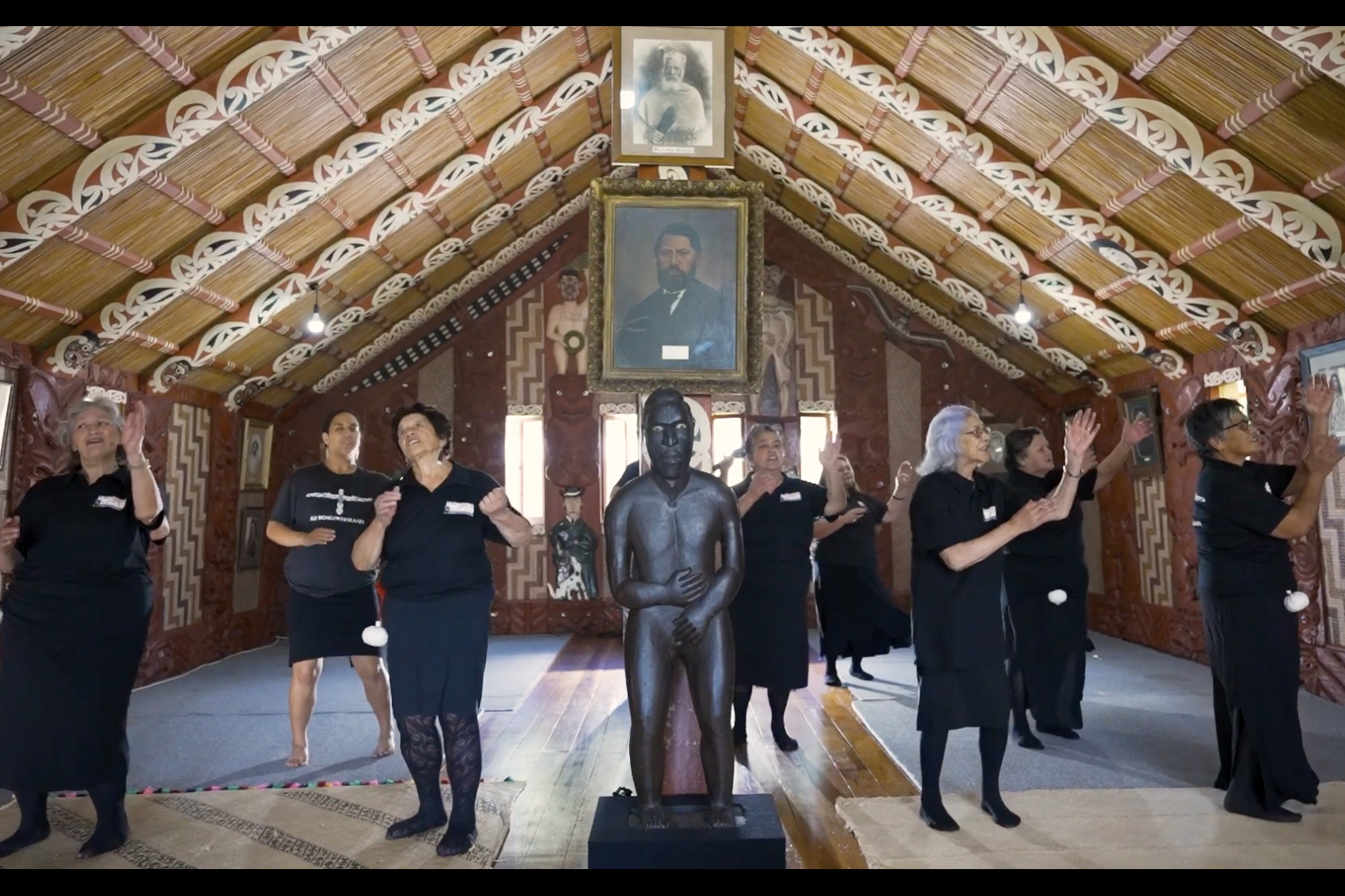 A group of people singing and doing actions in a hall with carvings and painting on the rafters