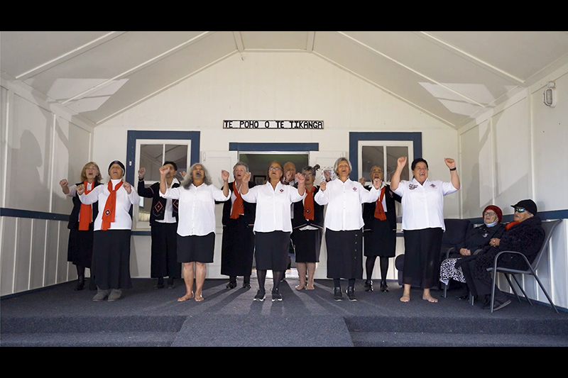 A group of women are singing an action song on the front porch of a hall