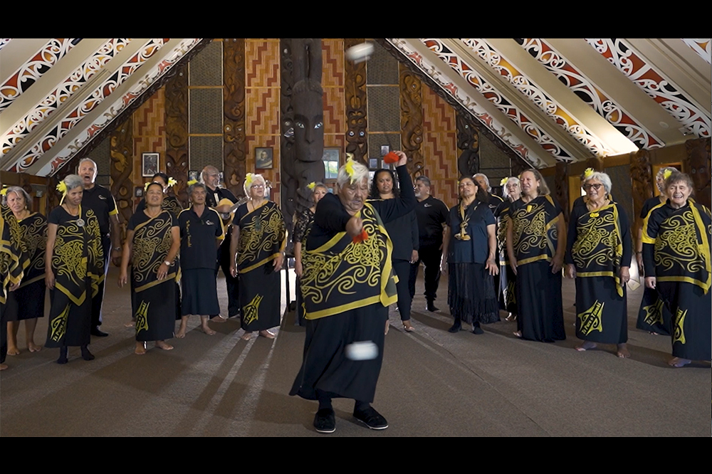 A group of people singing behind one woman doing an action song with poi (white balls on strings)