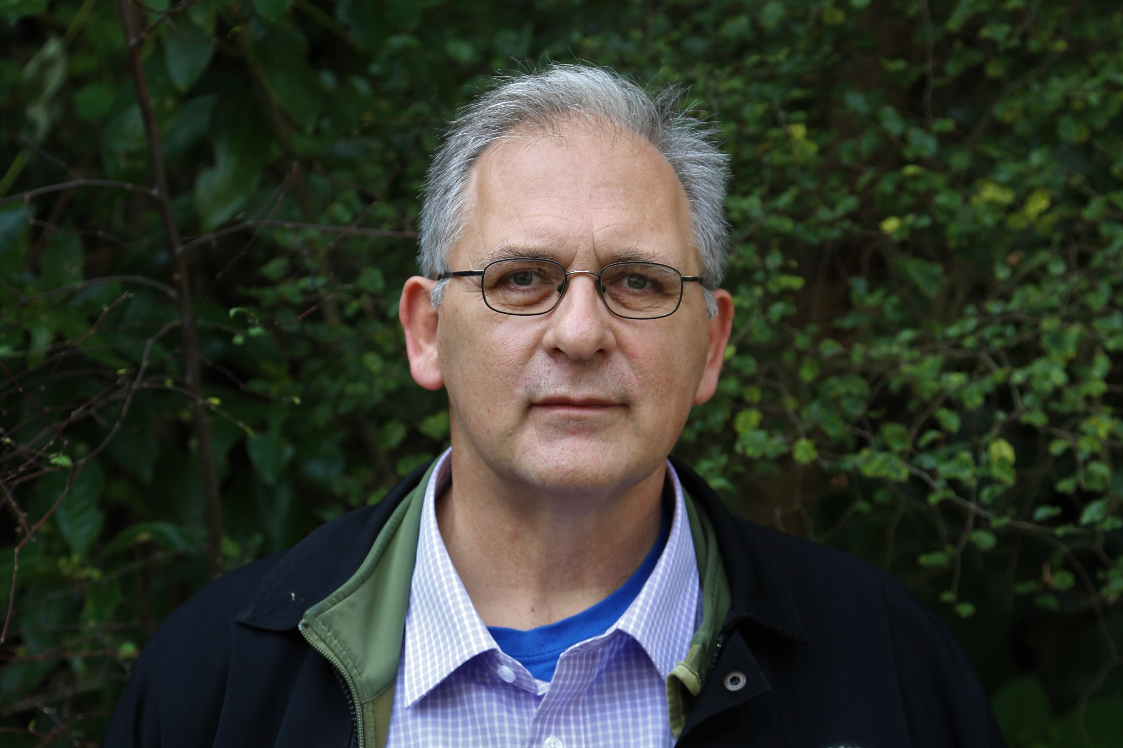 A head and shoulders photo of a man in front of a hedge