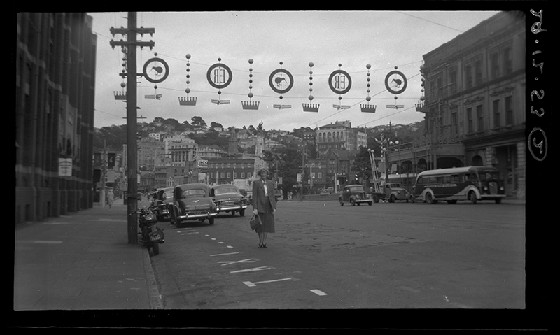 Black and white photo of a street set up for a parade with a woman standing in the middle of it