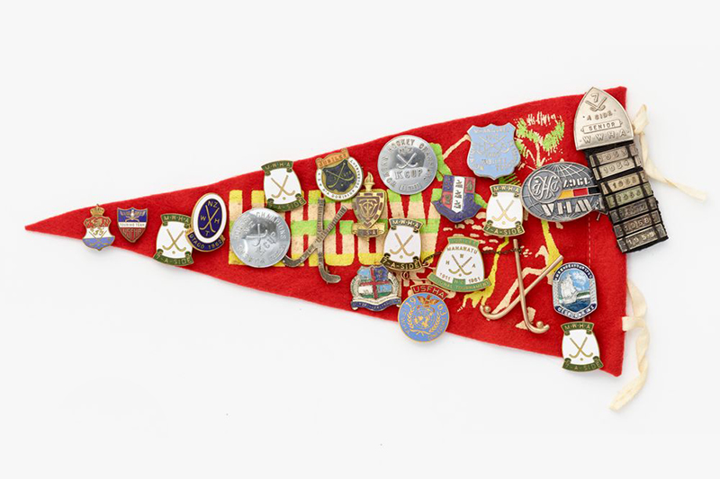 A red felt triangle flag covered in metal and enamel badges for sport