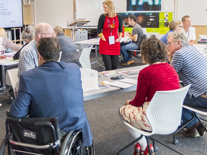Accessibility workshop, Nature Renewal project, 2018. Photo by Rachael Hockridge. Te Papa (105327) A room where people are sitting at tables in a workshop. One person is sitting in a wheelchair