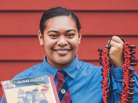 Mele Haunga, 2017. Photo by Amanda Rogers. Te Papa A teenage girl in a school uniform holding pandanus seed necklace and a booklet, standing in front of a dark red wooden wall