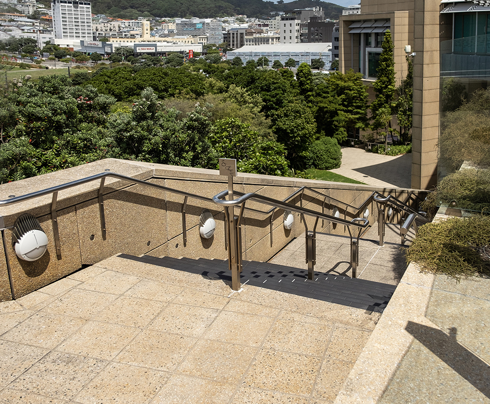 Looking down on a outdoor staircase leading up from a crop of trees, on the side of a building.