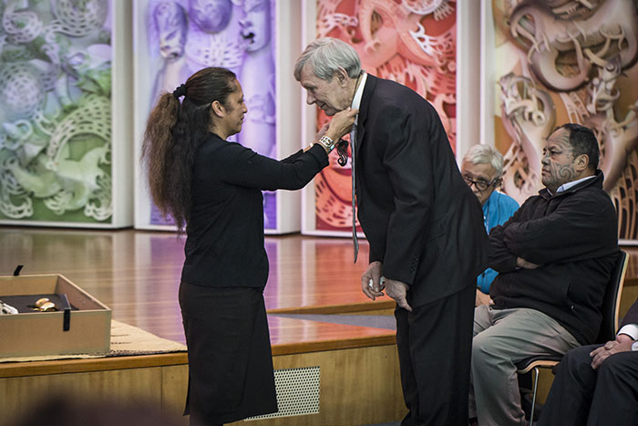 A woman places a necklace around Sir Peter Snell's neck