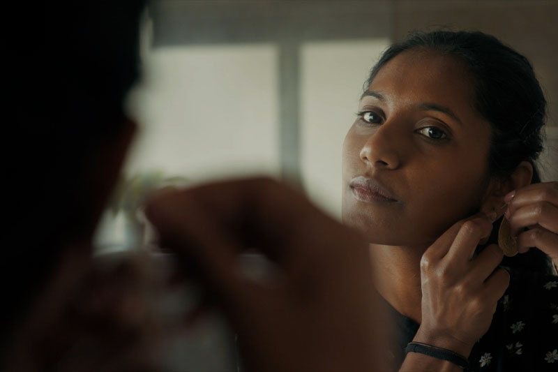 Photo of a woman looking into mirror, putting on an earring.