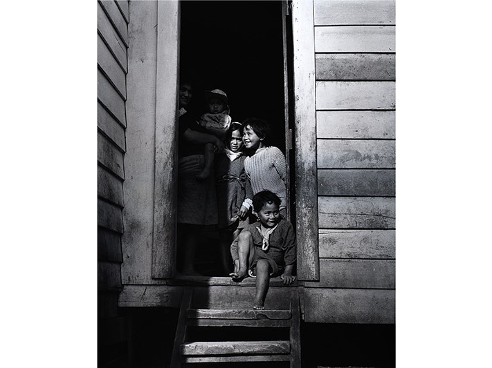 Ans Westra, Washday at the pa, front cover image. From the series: Washday at the pa. Ruatoria, 1964. Purchased 1993 with New Zealand Lottery Grants Board funds. Te Papa (O.002336/01) Cover image for Washday at the pa. A black and white photo of children sitting and standing on the doorstep of a house