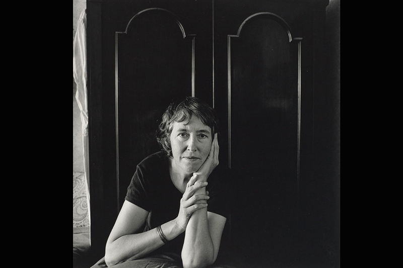 A black and white portrait of a woman looking at the camera with her chin resting on her hand.