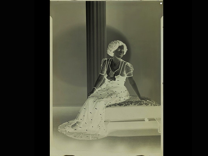 Negative of Miss A Savage – view the final image on Miss A Savage, 1940, Wellington, by Spencer Digby Studios. Spencer Digby / Ronald D Woolf Collection. Gift of Ronald Woolf, 1975. Te Papa (B.068904) Negative of view of a photograph of a woman in a long dress sitting on a settee.