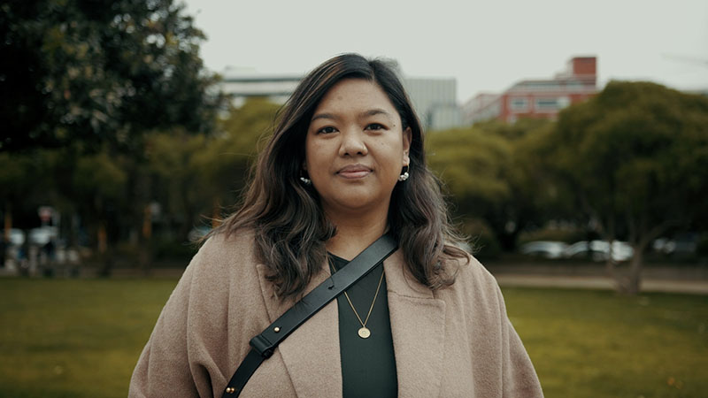 A woman stands in a park looking into the camera on an overcast day