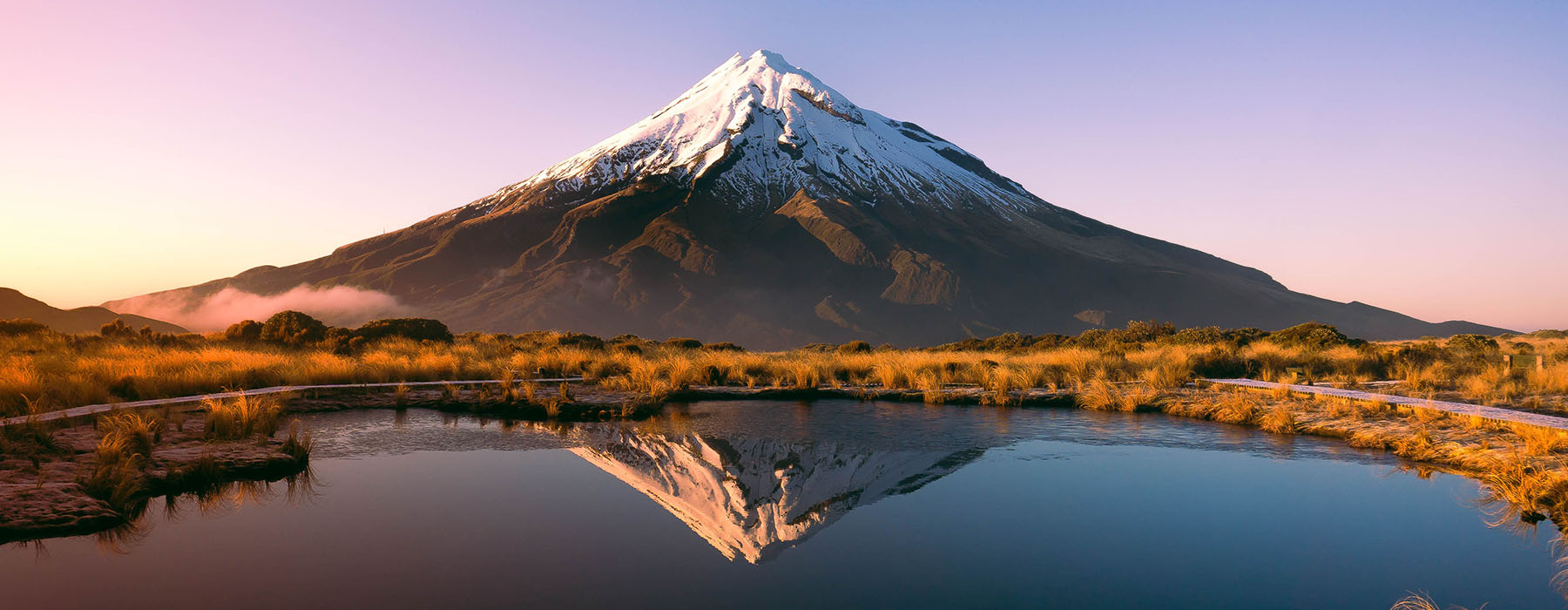 View of conical Mt Taranaki, with a body of water in front of it reflecting the mountain