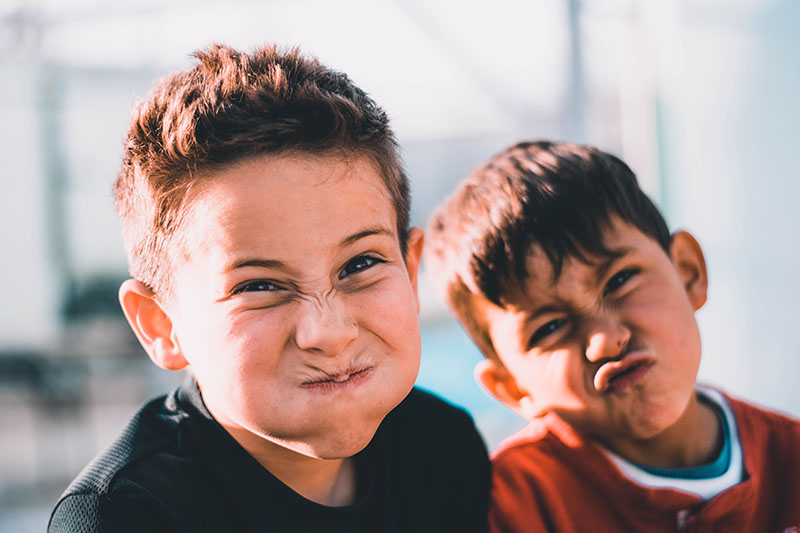 Two young boys scrunch up their faces at the camera