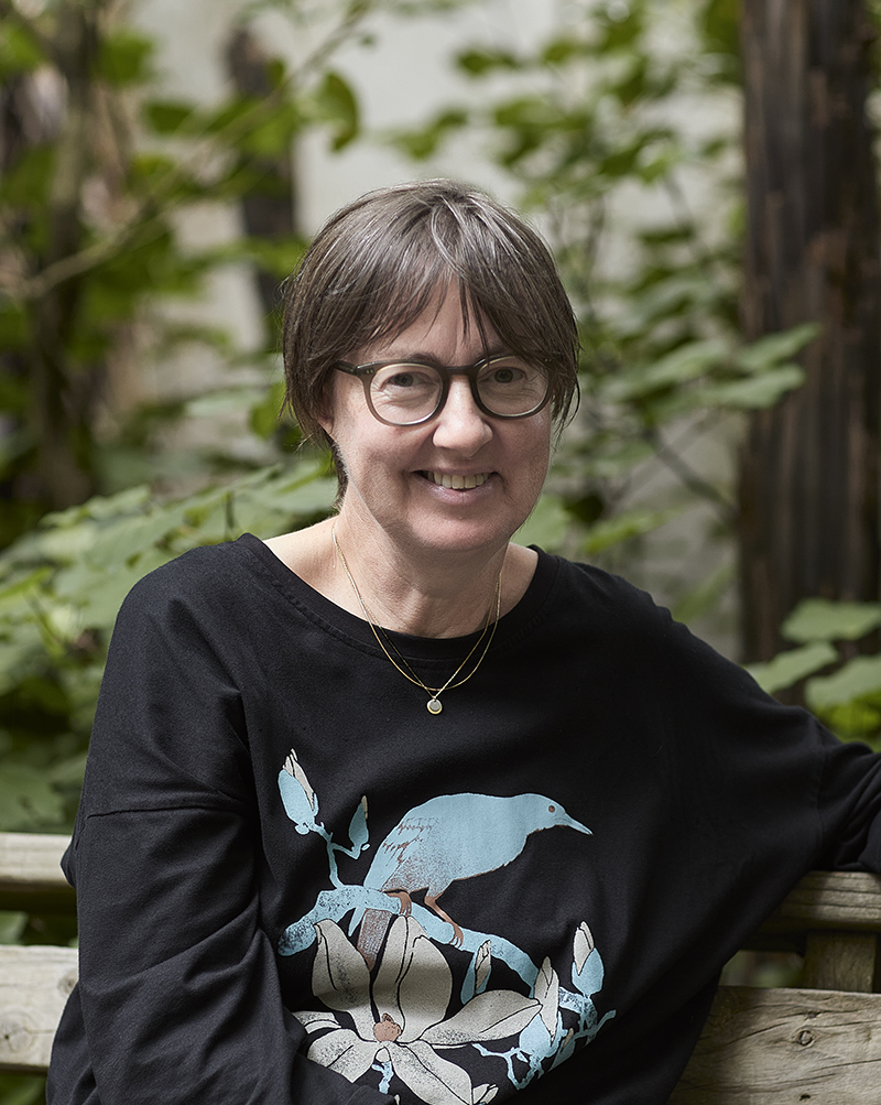 A woman in glasses is sitting and smiling at the camera.