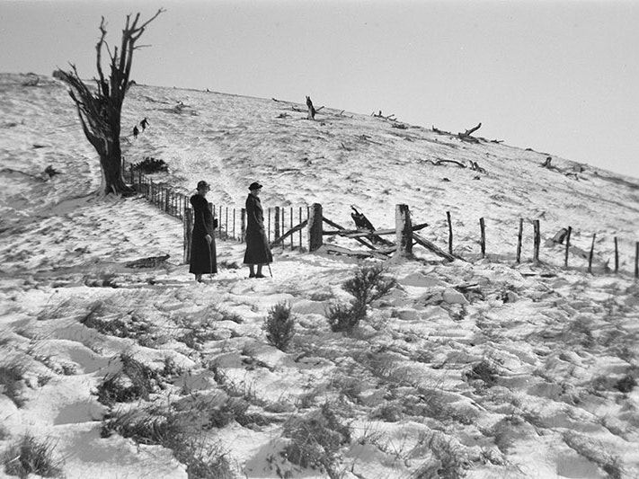 Deep snow and vestiges of the former forest, 2 August 1936, by Leslie Adkin. Gift of G. L. Adkin family estate, 1964. Te Papa (A.007126) Two women in formal coats and hats stand for a photo in a field covered in snow, beside a fence