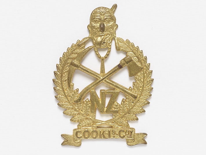 Cook Island Company Badge 1916, New Zealand, maker unknown. Purchased 2020. CC BY-NC-ND 4.0. Te Papa (FE013568) New Zealand Pioneer Battalion Badge and features the face of a Maori warrior wearing a solid necklace that joins the tips of two ferns. Crossed over in the centre is an axe and a pickaxe. "NZ" (an abbreviation of New Zealand) appears below the warrior’s n