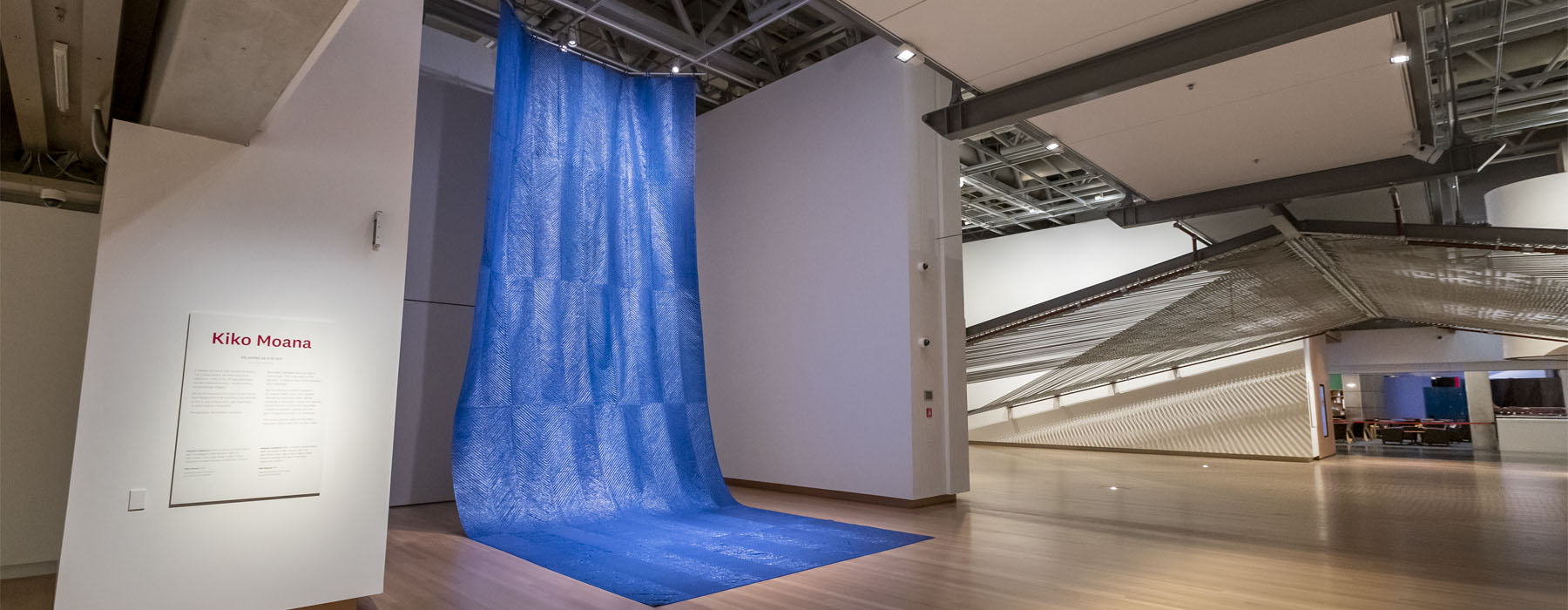 ‘Kiko Moana’ on display in Te Papa. A large sheet of blue tarpaulin hangs from the ceiling, and drapes onto the floor, resembling a waterfall