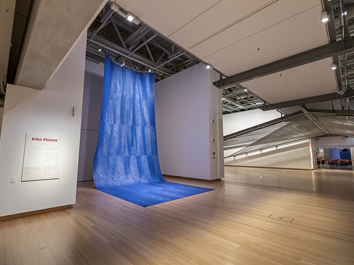 Mataaho Collective, Kiko Moana, 2016, polyethene tarpaulin and cotton thread. Te Papa (ME024286) ‘Kiko Moana’ on display in Te Papa. A large sheet of blue tarpaulin hangs from the ceiling, and drapes onto the floor, resembling a waterfall